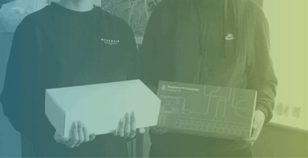 Close-up of two young adults wearing sweatshirts. They each hold Raspberry Pi boxes in front of their chests. Neither of their faces can be seen.