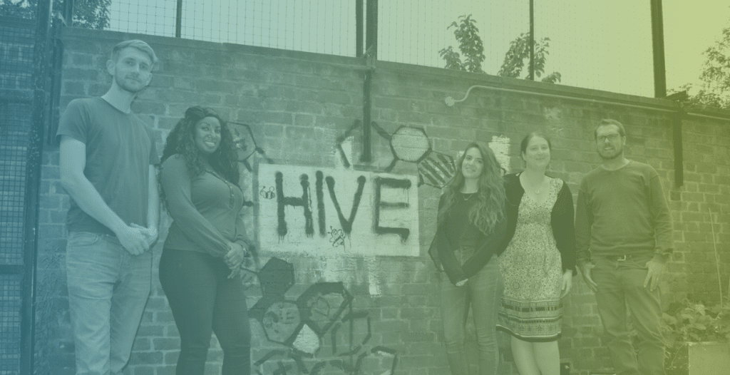 The Hive team stand in front of a wall with The Hive painted on it in a graffiti-style.